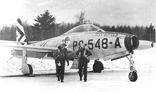 F-84B Thunderjet PS-548-A parked on tarmac with pilots standing nearby
